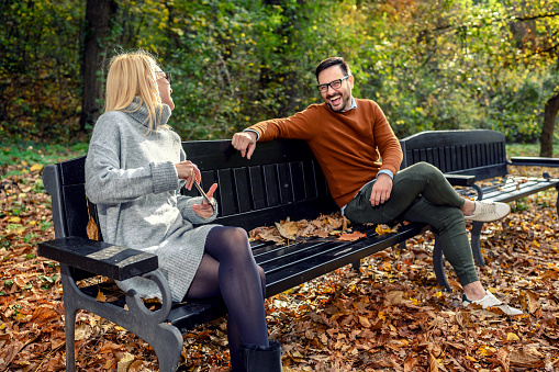 Woman and man in social distancing flirting sitting on a park bench