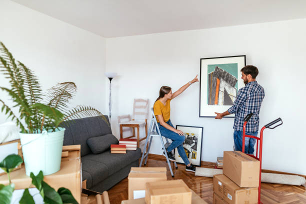 Couple moving in new apartment, woman and man putting picture on the wall Couple moving in the new apartment, unpacking cardboard boxes and moving the furniture in decorating stock pictures, royalty-free photos & images