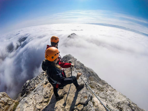 ヴィアフェラータを経由して霧の谷に続く登山家のカップル - 登山　夏 ストックフォトと画像