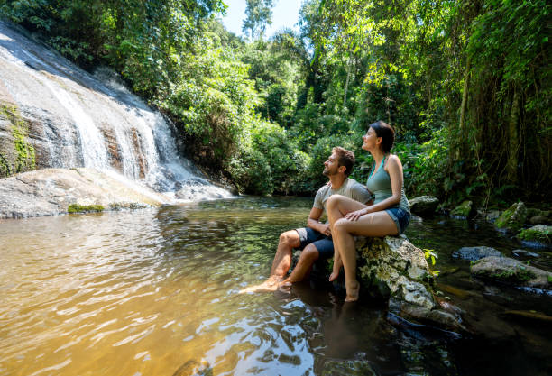 Couple of hikers looking at a beautiful waterfall Happy couple of hikers looking at a beautiful waterfall in Brazil and smiling â outdoors lifestyle concepts eco tourism stock pictures, royalty-free photos & images