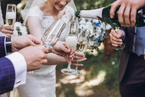 Couple of newlyweds, bride and groom together with bridesmaids and groomsmen drinking champagne outdoors hands closeup, wedding celebration with friends stock photo