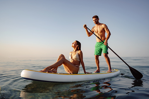 Couple of tourists young man and woman having fun paddleboarding at sea at sunset