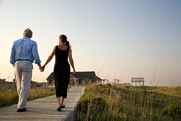 Couple on Boardwalk Couple walk hand in hand on a boardwalk towards a beach pavilion. Horizontal shot. north carolina beach stock pictures, royalty-free photos & images