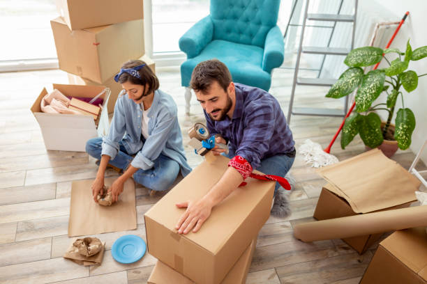 Couple packing things into cardboard boxes High angle view of a young couple in love sitting on the floor of their apartment, packing things into cardboard boxes, getting ready for relocation relocation stock pictures, royalty-free photos & images