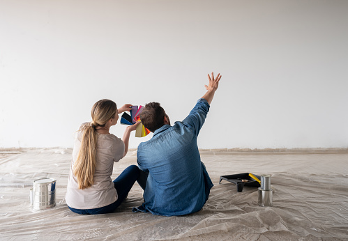 Happy couple painting their house and deciding on a color for their wall using a palette while sitting on the floor - home decor concepts