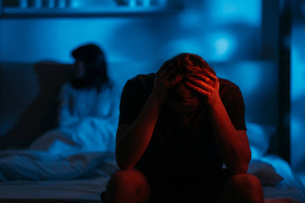 couple quarrel night conflict depressed man bed Couple quarrel. Night conflict. Divorce issue. Depressed devastated man clutching head sitting on bed on distance from offended wife in dark red blue neon light on defocused background. background of husband and wife in bed stock pictures, royalty-free photos & images