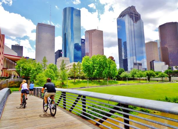 Couple Riding Bikes Across Bridge in Downtown Houston Park Young Man and Woman Riding Bikes on Small Wooden Bridge in Houston's Buffalo Bayou Park (view of river and skyline of downtown Houston) - Houston, Texas, USA swamp photos stock pictures, royalty-free photos & images