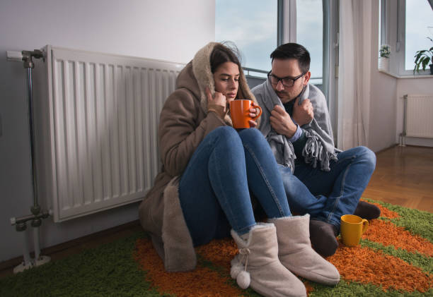 Couple sitting beside radiator Young couple in jacket and covered with blanket sitting on floor beside radiator and trying to warm up cold temperature stock pictures, royalty-free photos & images