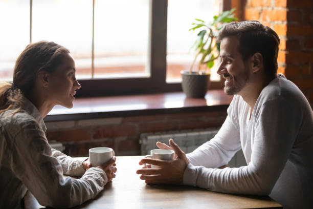 Couple sitting in cafe talking drinking tea or coffee Side view smiling biracial woman sitting at table in cafe with caucasian man couple talking in cozy coffeeshop drinking tea coffee. Heterosexual friends romantic relationships or speed dating concept dating stock pictures, royalty-free photos & images