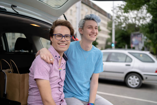 pareja lgbtq+ sentada en el maletero de su coche y abrazándose - pansexual fotografías e imágenes de stock