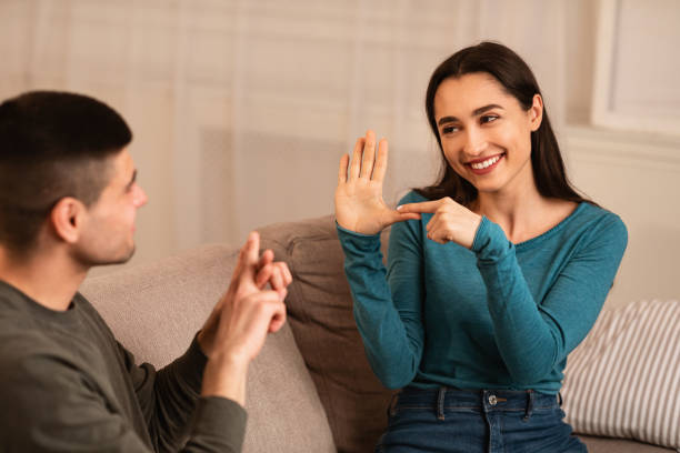 Couple Sitting On Sofa Communicating With Sign Language Smiling deaf and mute couple communicating at home using sign language, sitting on couch in living room sign language stock pictures, royalty-free photos & images