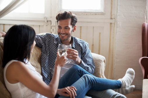 Couple sitting on sofa talking and toasting in wine in their cozy loft apartment