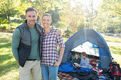 Couple smiling at camera while kids sitting in tent at campsite