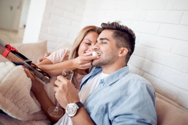 Couple spending their free time at home Portrait of young caucasian couple eating a heart chocolate cookie.Valentines couple sharing cookie,holds a glass of wine in hands. couple eating chocolate stock pictures, royalty-free photos & images
