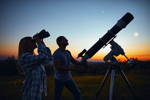 Couple stargazing together with a astronomical telescope.