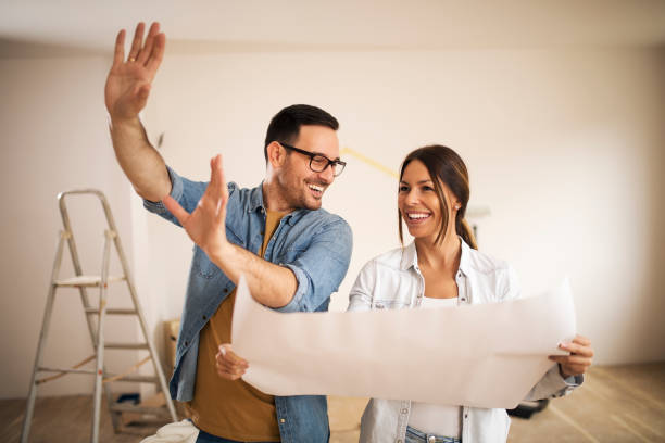 Couple talking about home decoration Young couple standing in their apartment while woman holding blueprint and man showing to her new ideas. home improvement stock pictures, royalty-free photos & images