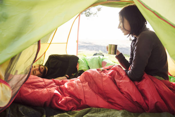 Couple traveling, spending time in tent, drinking coffee in the morning Two friend traveling and spending time in tent while drinking coffee in the morning. Happy people in camping. View from inside. Couple of travelers camping sleeping bags stock pictures, royalty-free photos & images