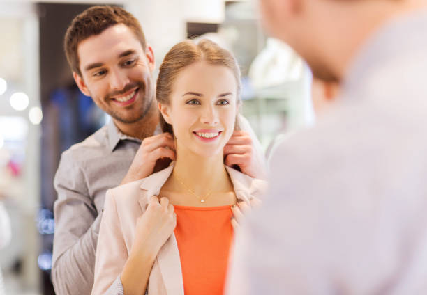 couple trying golden pendant on at jewelry store stock photo