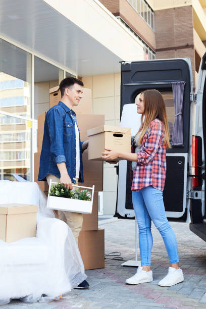 Side view portrait of young happy woman unloading boxes from moving...