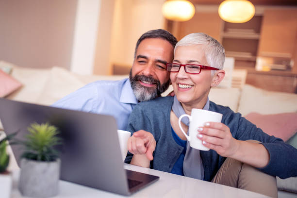 Couple using laptop at home Happy mature couple enjoying in their coffee time in the living room. mature couple stock pictures, royalty-free photos & images