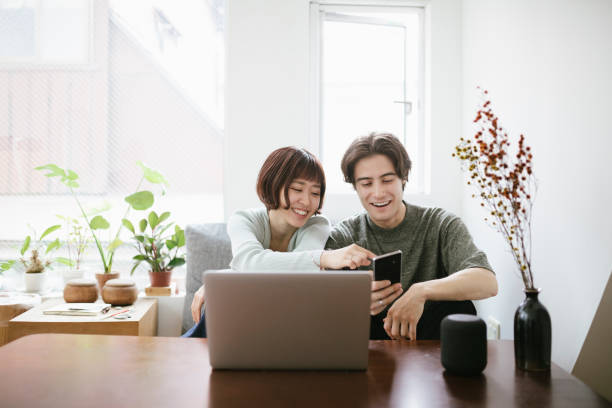 Couple Using Technology Together Couple sitting behind a coffee table, installing virtual assistant. electrical equipment photos stock pictures, royalty-free photos & images
