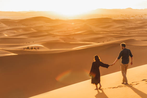 Couple walking in Sahara desert at sunset. View from behind, nature background. Travel, freedom and wanderlust concept. stock photo