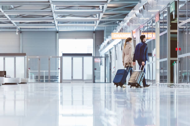 couple walking with luggage inside airport terminal - airport lounge imagens e fotografias de stock