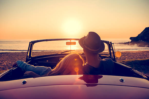 couple watching the sunset in a convertible car. - zonsondergang stockfoto's en -beelden