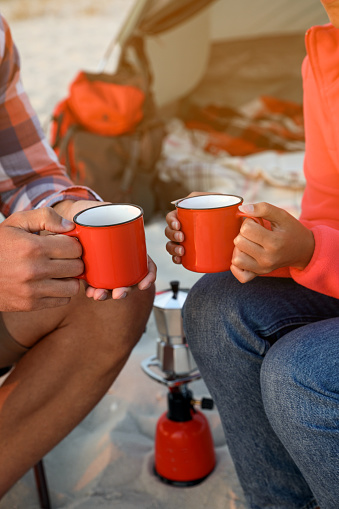 Couple with cups of hot drinks outdoors, closeup. Beach camping