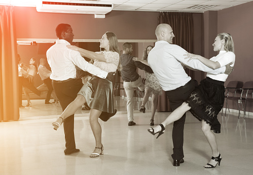 Adult dancing couples enjoying active boogie-woogie in modern studio