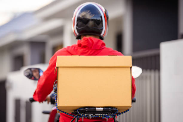 Courier in red uniform with a delivery box on back riding a motorcycle check the address to deliver food to the customer.
 Courier on a motorcycle delivering food in the city. stock photo
