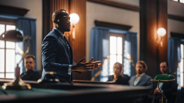 Court of Justice and Law Trial: Male Public Defender Presenting Case, Making Passionate Speech to Judge, Jury. African American Attorney Lawyer Protecting Client's Innocents with Supporting Argument. stock photo