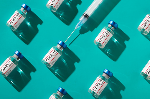 Covid 19 coronavirus vaccine vials with syringe repetition pattern with trendy lighting on teal background