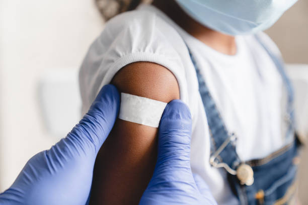 Covid 19 measles, ebola vaccinated. Doctor pediatrician injecting making vaccine to little african girl in medical clinic. Nurse applying medical patch after injection stock photo