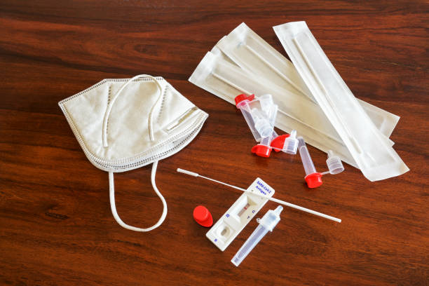 Covid-19 rapid antigen self test kit with negative result, nasal swabs, tubes, detection device and a surgical ffp-2 face mask on a brown wooden table, copy space, high angle view from above stock photo