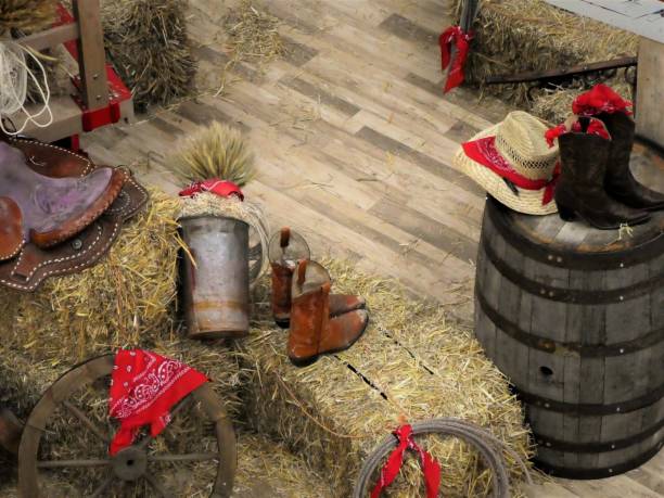 Cowboy Boots, Hats, Saddle and Straw Bales Surrounding a Barn Floor stock photo