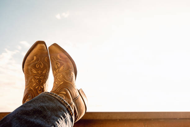 cowboy boots cowboy resting legs with feet crossed - sky background - negative space - boots country and western music stock pictures, royalty-free photos & images