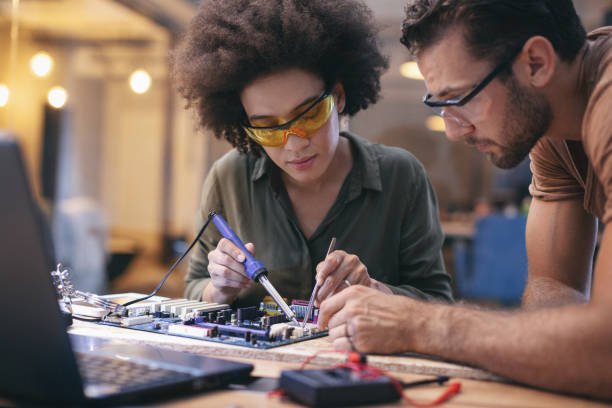 Co-workers working late on a circuit boards in office stock photo