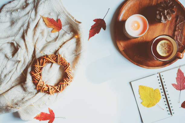 cozy autumn table, top view of still life details in hygge style on white background. Tea with lemon, woolen sweater, dried leaves and notepad. stock photo