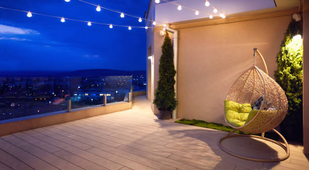cozy rooftop terrace with rattan hanging chair, garlands and beautiful landscape at night stock photo