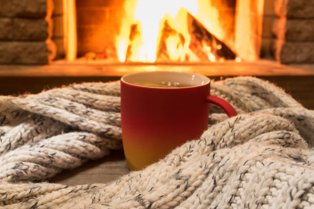 Cozy scene near fireplace with a Red cup with hot tea and cozy warm scarf. stock photo