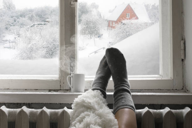 Cozy winter still life Cozy winter still life: woman legs in warm woolen socks under shaggy blanket and mug of hot beverage on old windowsill against snow landscape from outside. hygge stock pictures, royalty-free photos & images