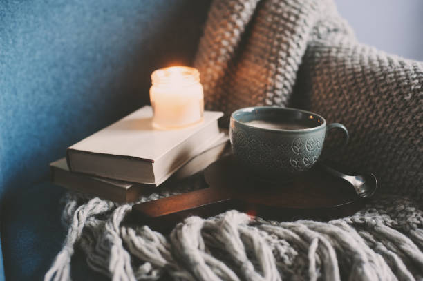 Cozy winter weekend at home. Morning with coffee or cocoa, books, warm knitted blanket and nordic style chair. Hygge concept. stock photo