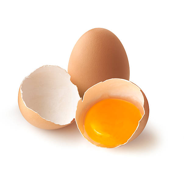 A cracked, brown egg next to a whole one Broken egg on white background egg yolk photos stock pictures, royalty-free photos & images