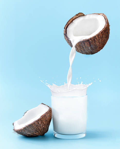 Cracked coconut with splashes of milk on blue background. coconut milk is poured into the glass Cracked coconut with splashes of milk on blue background. coconut milk is poured into the glass. coconut milk stock pictures, royalty-free photos & images