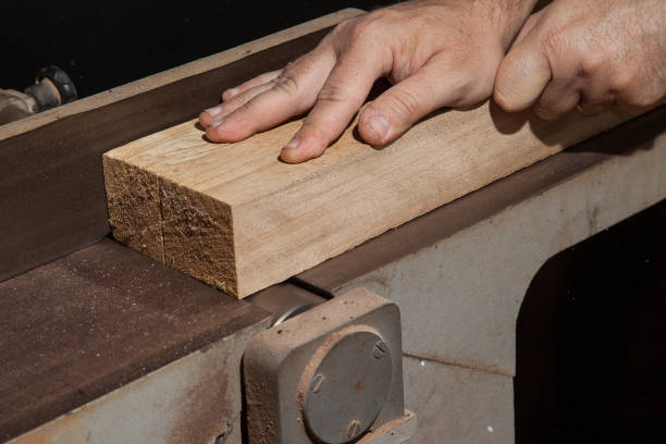 A craftsman flattening a wooden plank in electric table planer A craftsman flattening a wooden plank in electric table planer oficina stock pictures, royalty-free photos & images