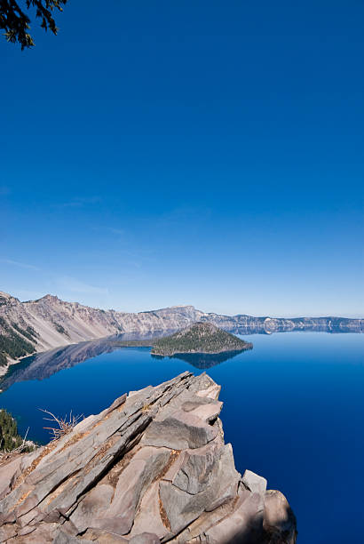 Rock Outcrop Overlooking Crater Lake Crater Lake exists in the blown-out caldera of a once mighty volcano known as Mount Mazama. This view of the lake with its calm blue water was taken from the Rim Trail in Crater Lake National Park, Oregon, USA. jeff goulden crater lake national park stock pictures, royalty-free photos & images
