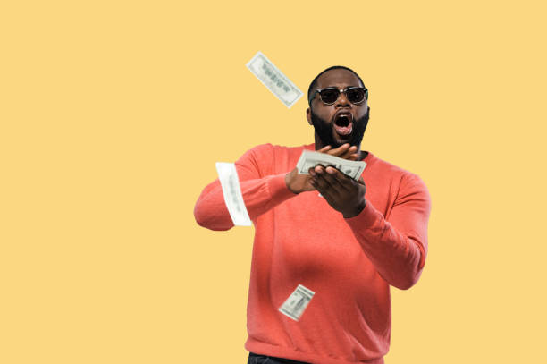 Crazy happy african american guy in sunglasses throws money standing on isolated yellow background stock photo