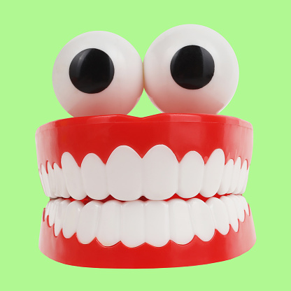 Here are artificial teeth jaws with eyeballs funny item isolated on bright green background.