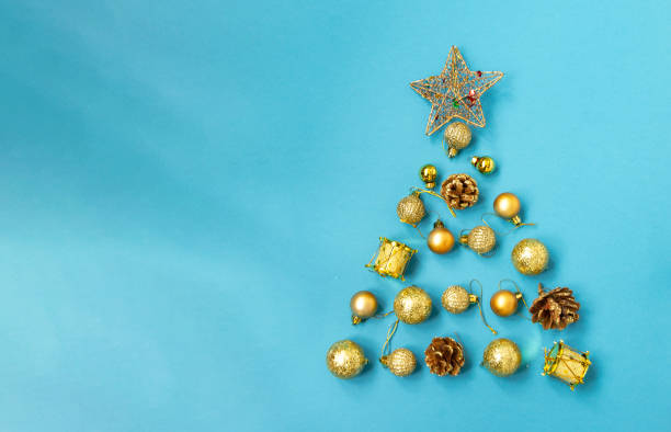 Creative Christmas tree made of gold baubles and a star, pine cones, balls on a blue background, copy space. Minimal, new year concept. top view, flat lay. stock photo
